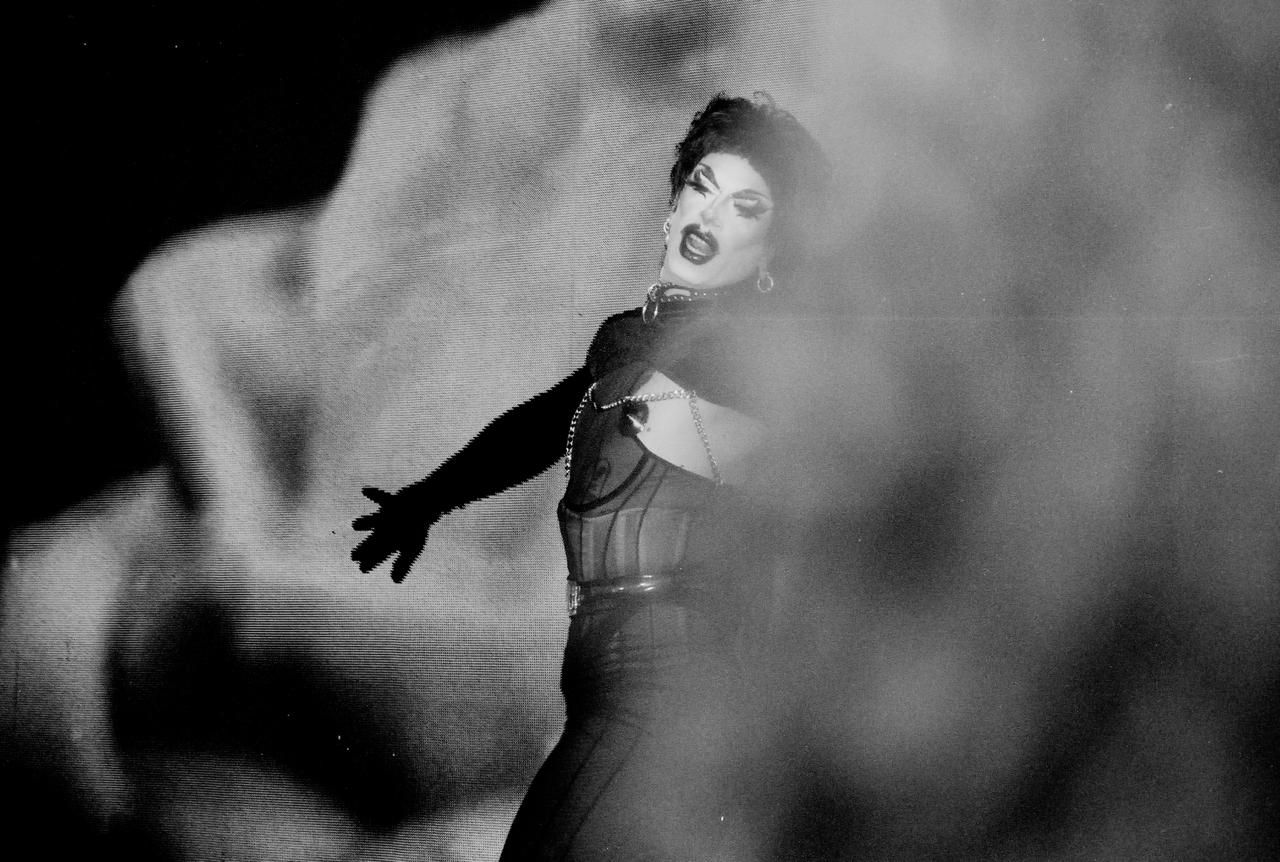 Artiste drag sur scène, bras tendu, gant noir, dans la fumée.
